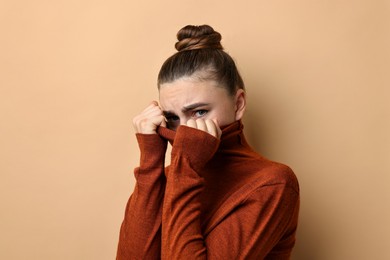 Photo of Scared young woman hiding on beige background