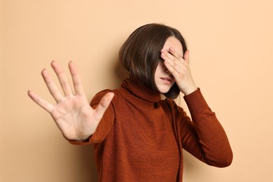 Photo of Scared young woman hiding on beige background