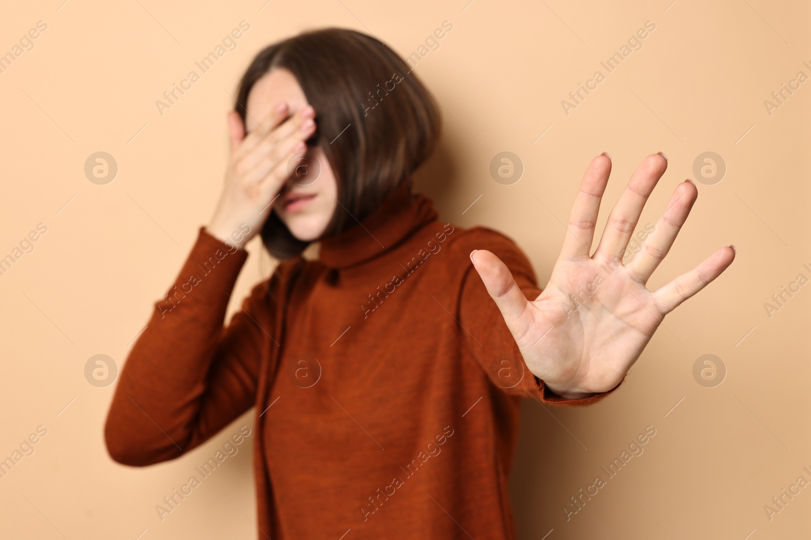 Photo of Scared young woman hiding on beige background, selective focus