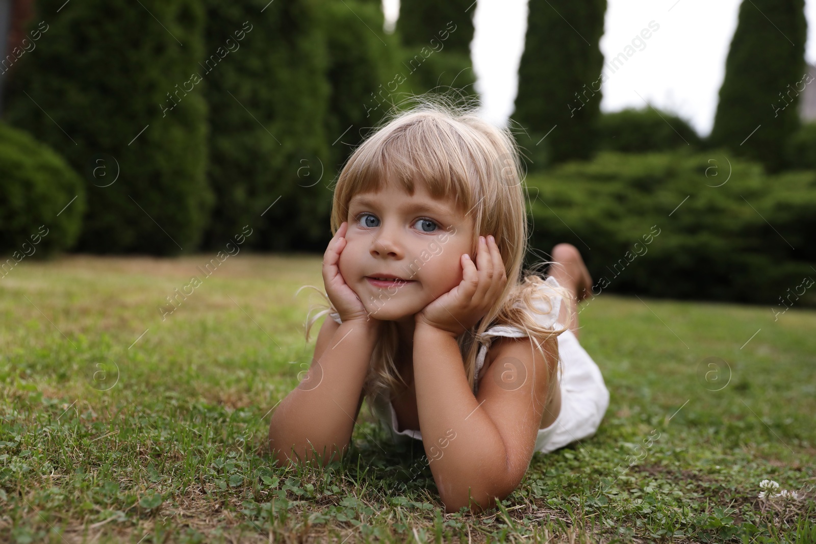 Photo of Cute little girl on green grass outdoors. Child enjoying beautiful nature