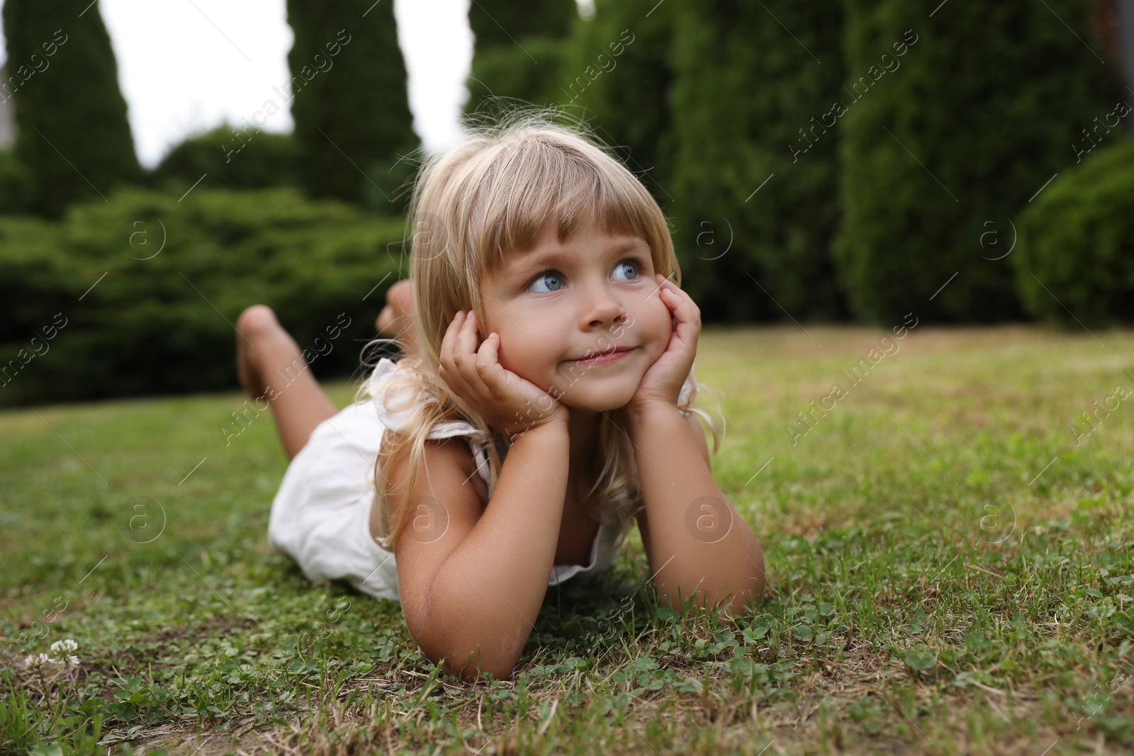 Photo of Cute little girl on green grass outdoors. Child enjoying beautiful nature