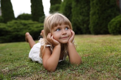 Photo of Cute little girl on green grass outdoors. Child enjoying beautiful nature