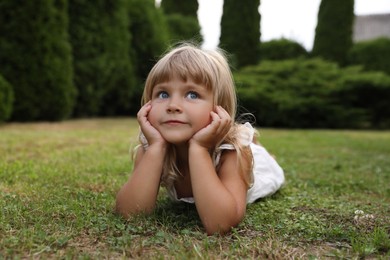 Photo of Cute little girl on green grass outdoors. Child enjoying beautiful nature