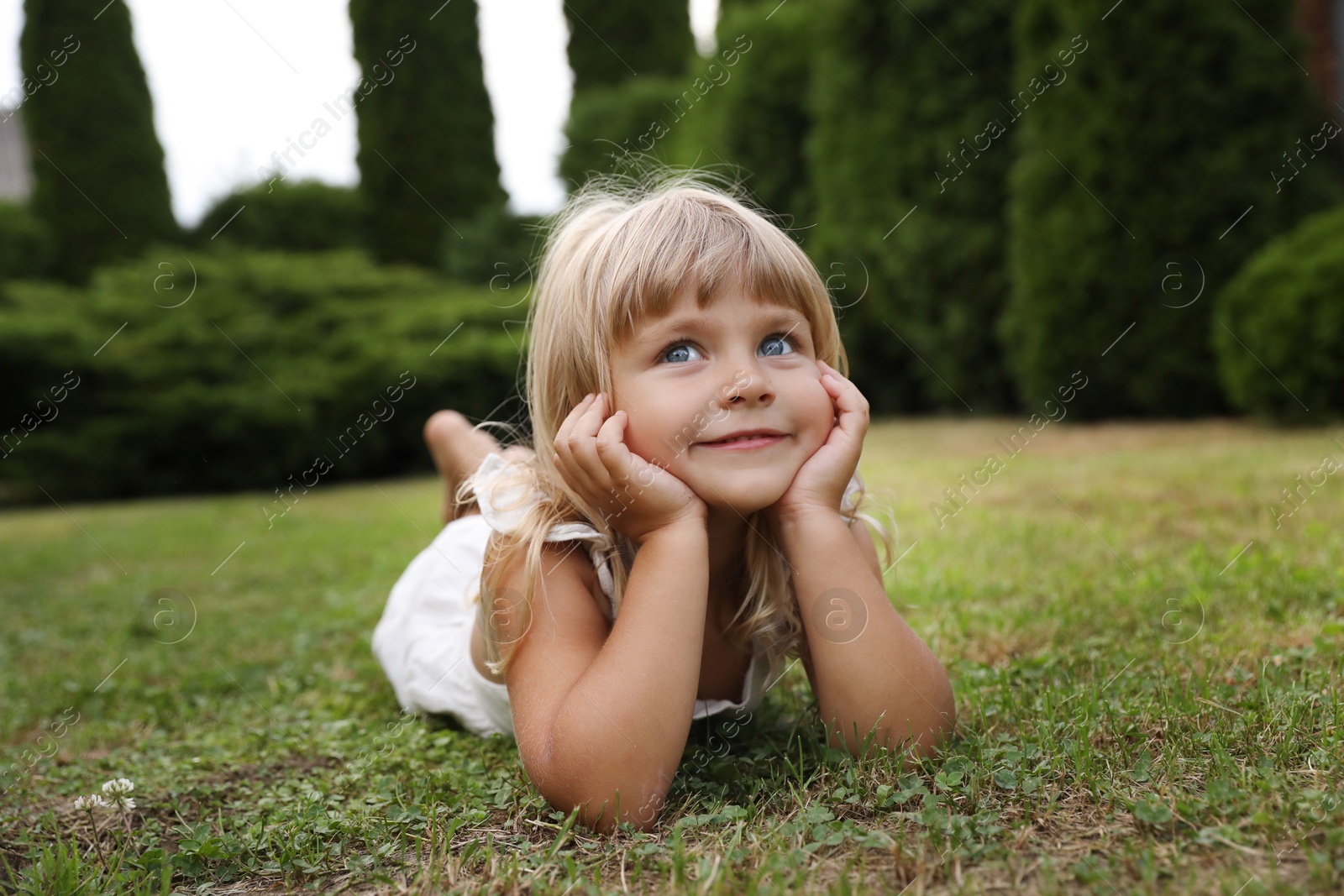 Photo of Cute little girl on green grass outdoors. Child enjoying beautiful nature