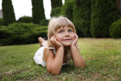 Photo of Cute little girl on green grass outdoors. Child enjoying beautiful nature