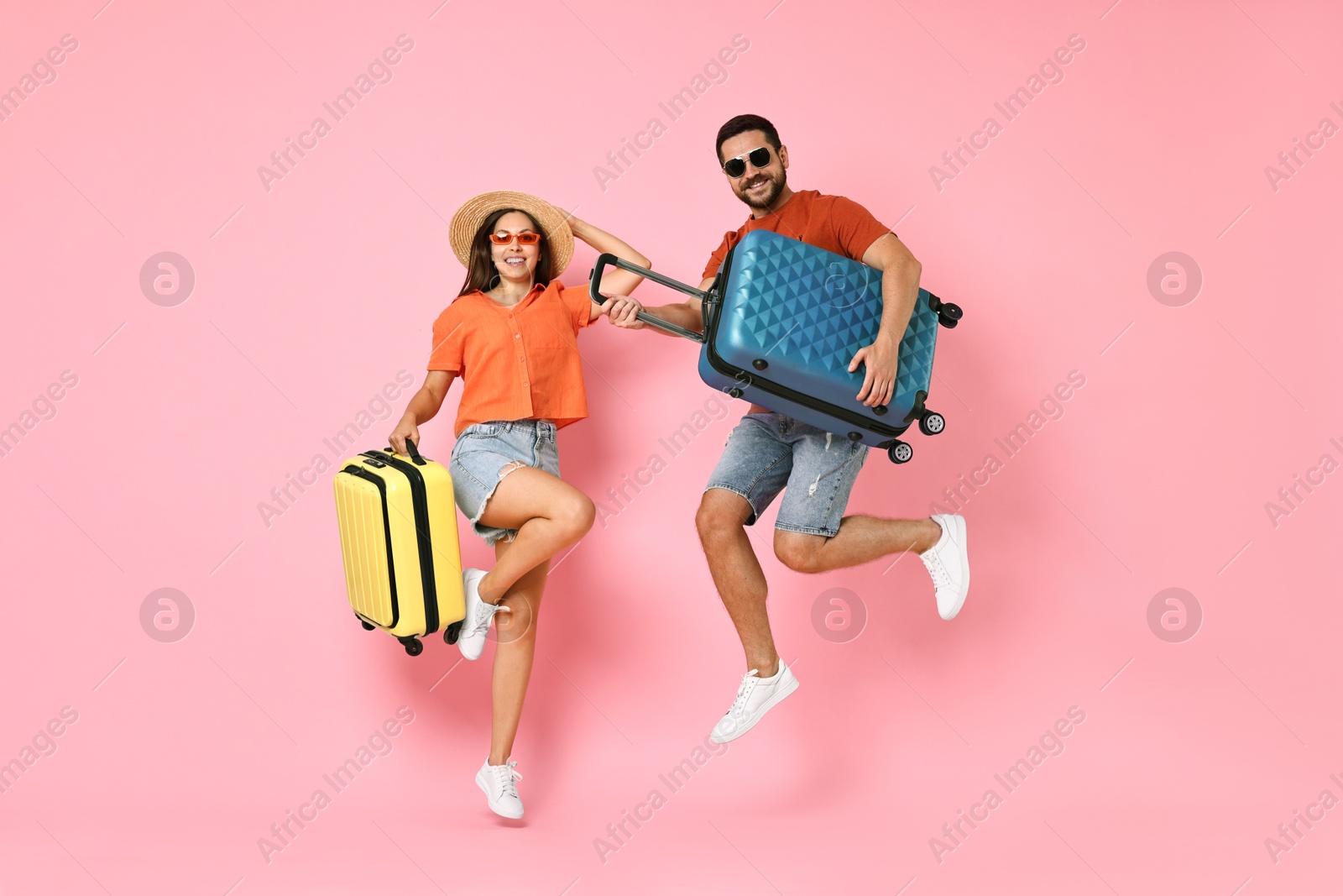 Photo of Happy woman and man with suitcases jumping on pink background