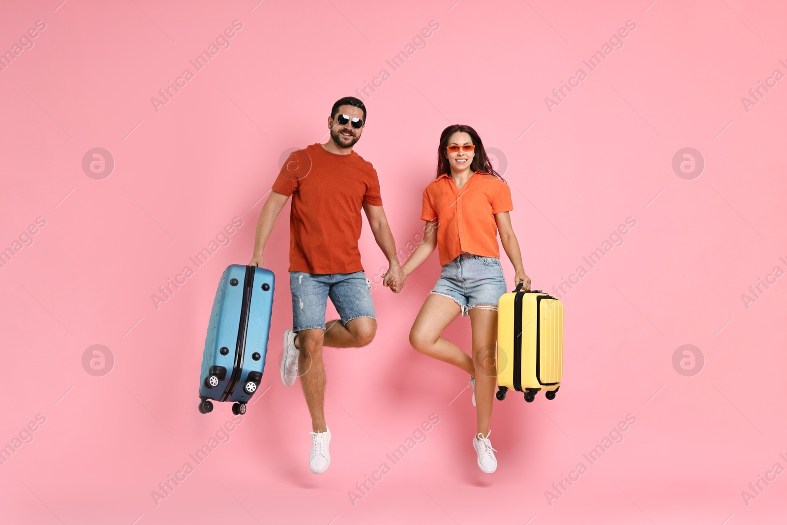 Photo of Happy woman and man with suitcases jumping on pink background