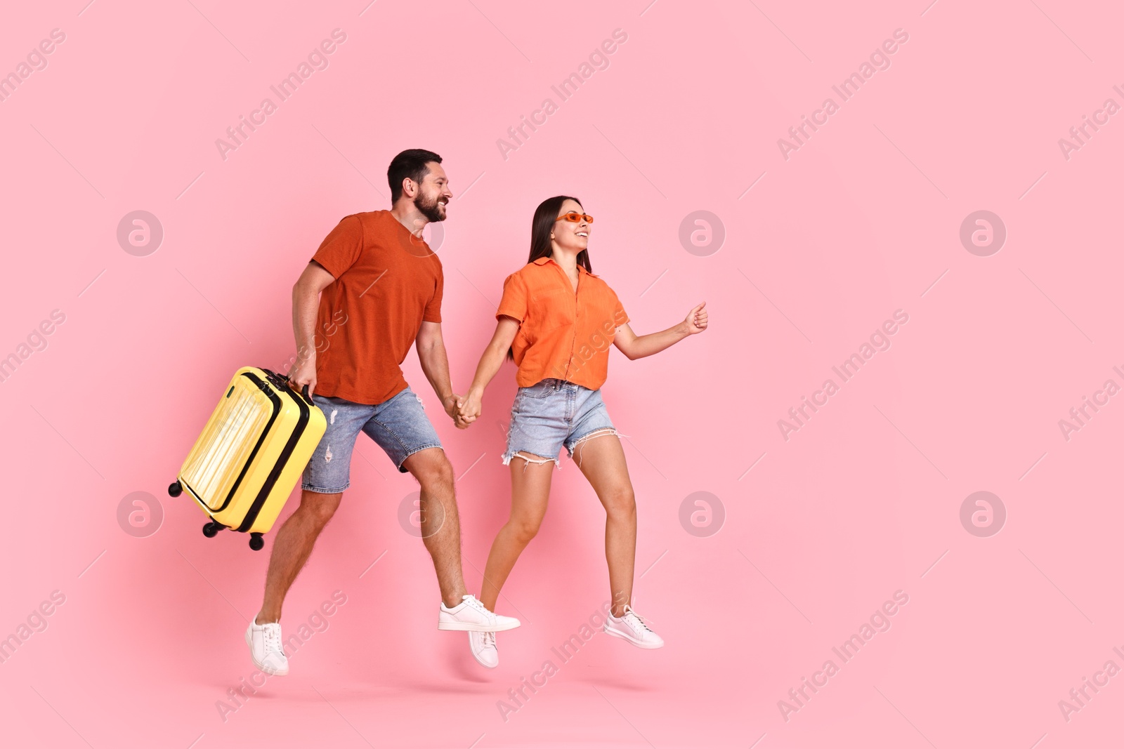 Photo of Happy woman and man with suitcase jumping on pink background