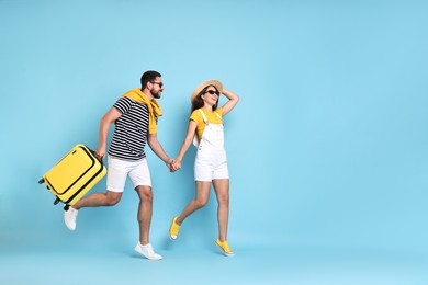 Photo of Happy couple with suitcase running on light blue background