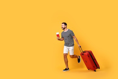 Photo of Happy man with suitcase, passport and ticket running on orange background, space for text