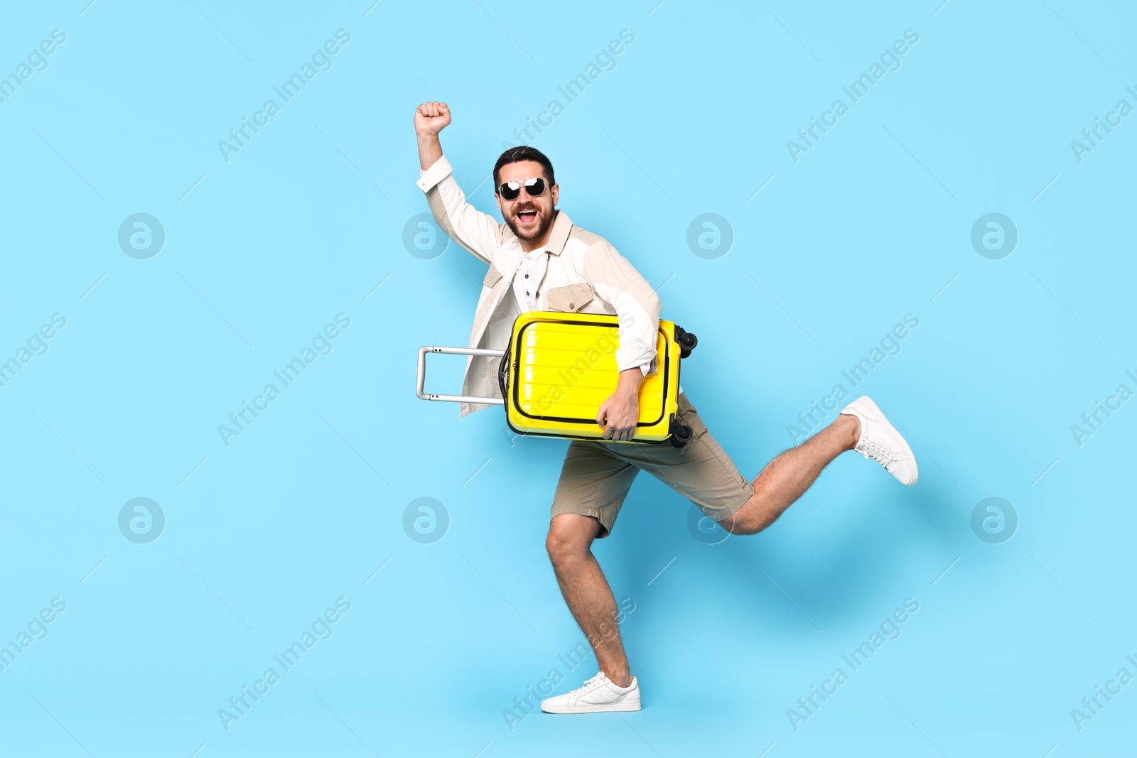 Photo of Happy man in sunglasses with suitcase on light blue background