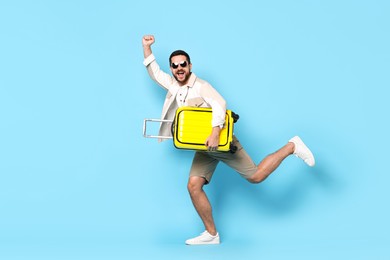 Photo of Happy man in sunglasses with suitcase on light blue background