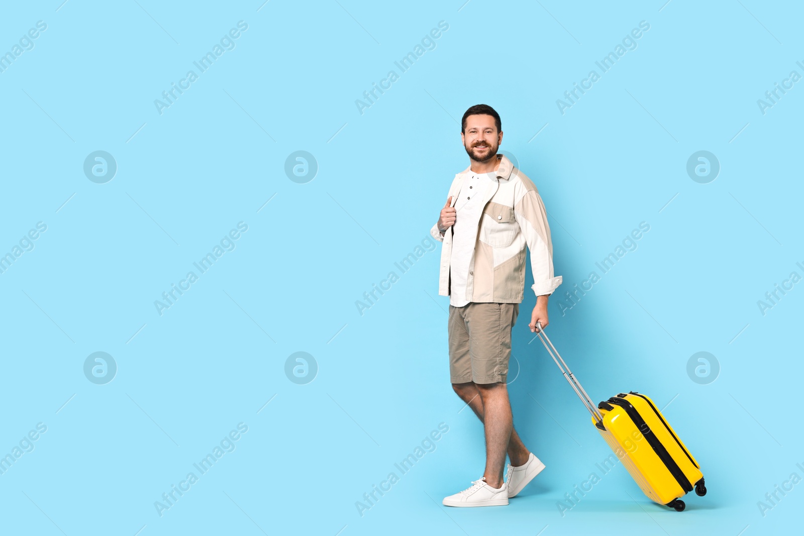 Photo of Happy man with suitcase on light blue background, space for text