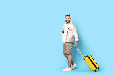 Photo of Happy man with suitcase on light blue background, space for text