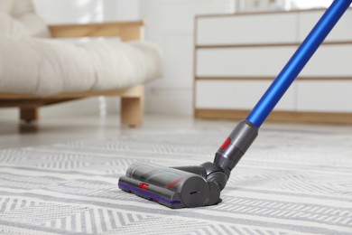 Photo of Cleaning carpet with cordless vacuum cleaner indoors, closeup. Space for text