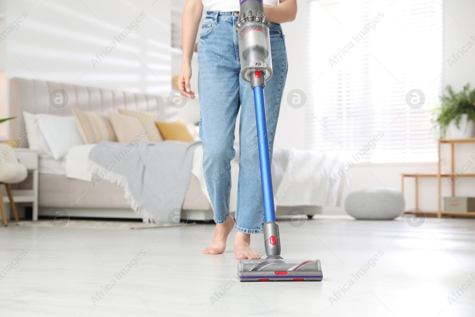 Photo of Woman cleaning floor with cordless vacuum cleaner indoors, closeup