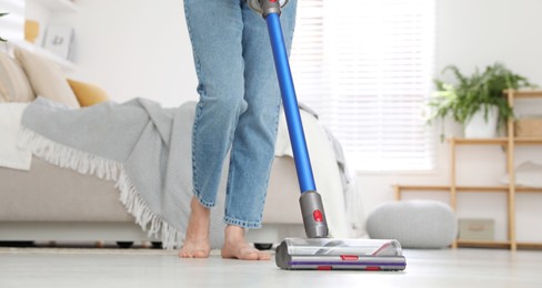 Photo of Woman cleaning floor with cordless vacuum cleaner indoors, closeup