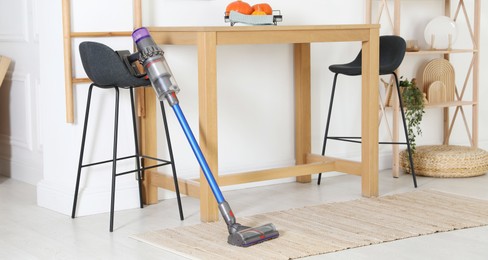 Photo of One cordless vacuum cleaner leaning on stool indoors