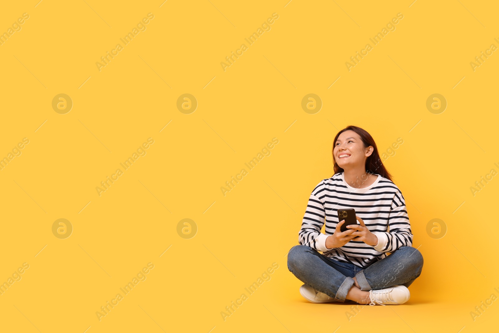 Photo of Smiling young woman with smartphone on yellow background. Space for text