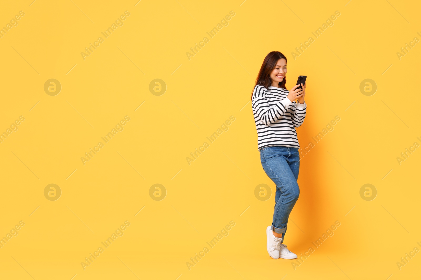 Photo of Smiling young woman using smartphone on yellow background. Space for text