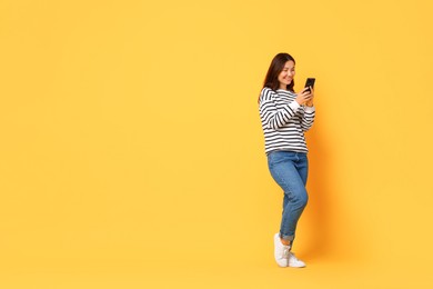 Photo of Smiling young woman using smartphone on yellow background. Space for text