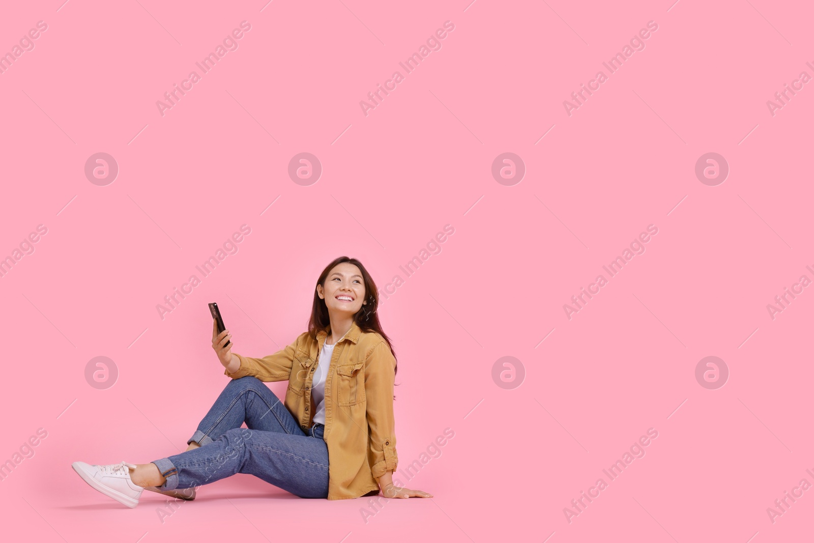 Photo of Smiling young woman with smartphone on pink background. Space for text