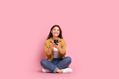 Photo of Smiling young woman with smartphone on pink background