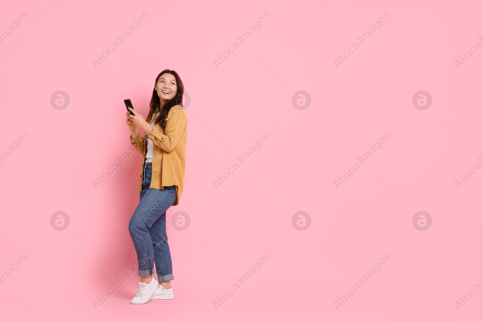 Photo of Smiling young woman with smartphone on pink background. Space for text