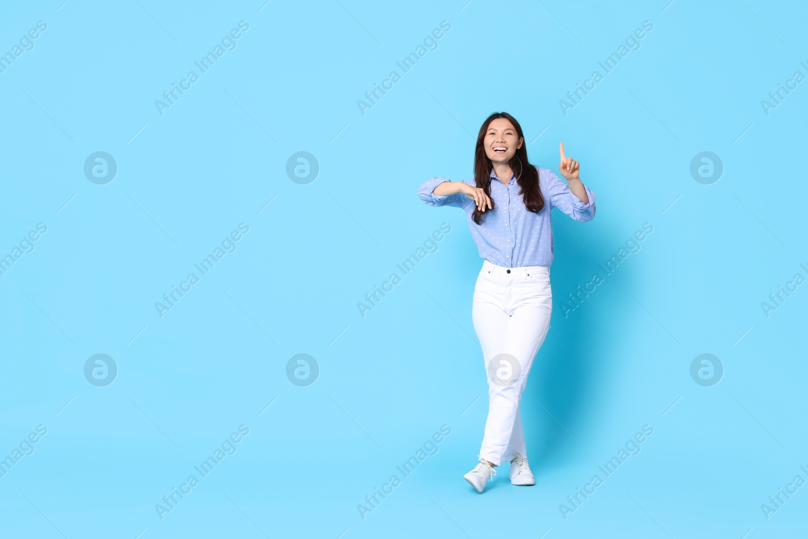 Photo of Smiling woman pointing at something on light blue background. Space for text