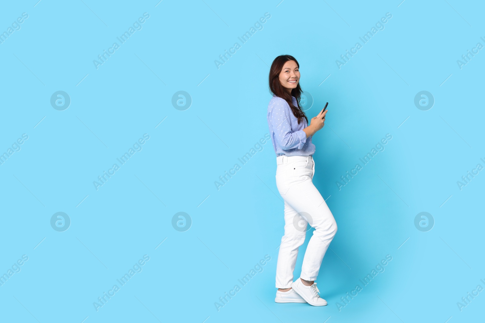 Photo of Smiling woman with smartphone on light blue background. Space for text