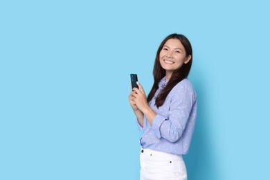 Photo of Smiling woman with smartphone on light blue background. Space for text