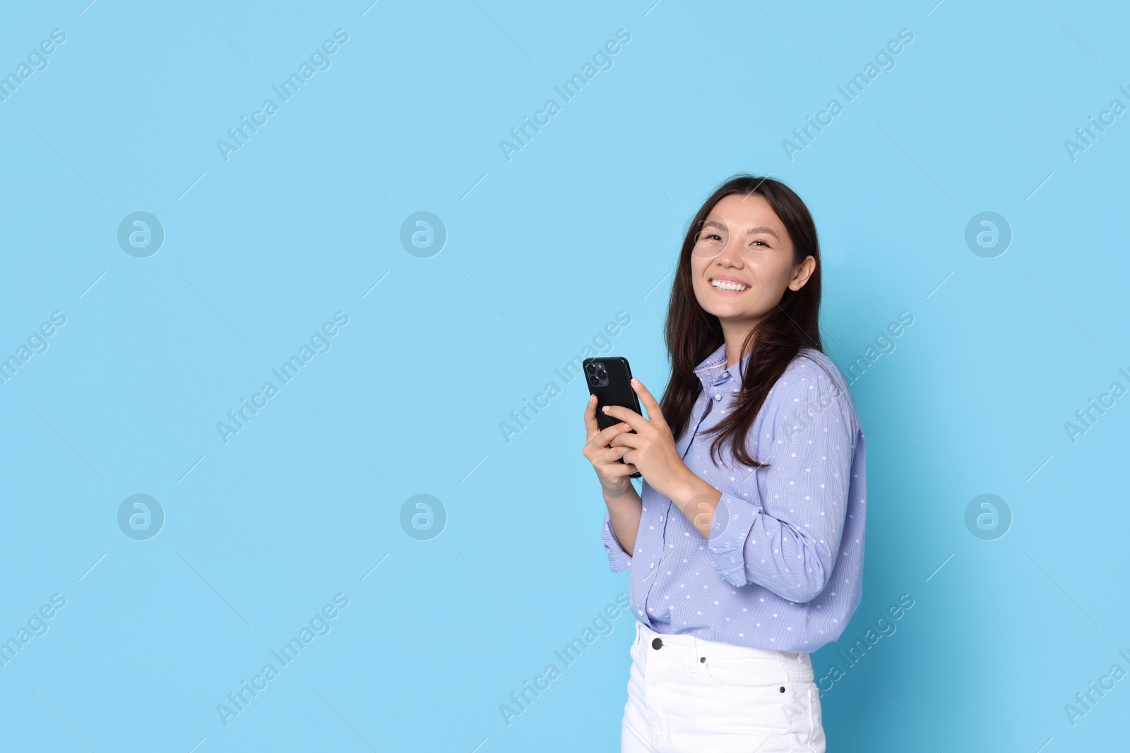 Photo of Smiling woman with smartphone on light blue background. Space for text