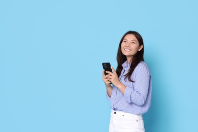 Photo of Smiling woman with smartphone on light blue background. Space for text