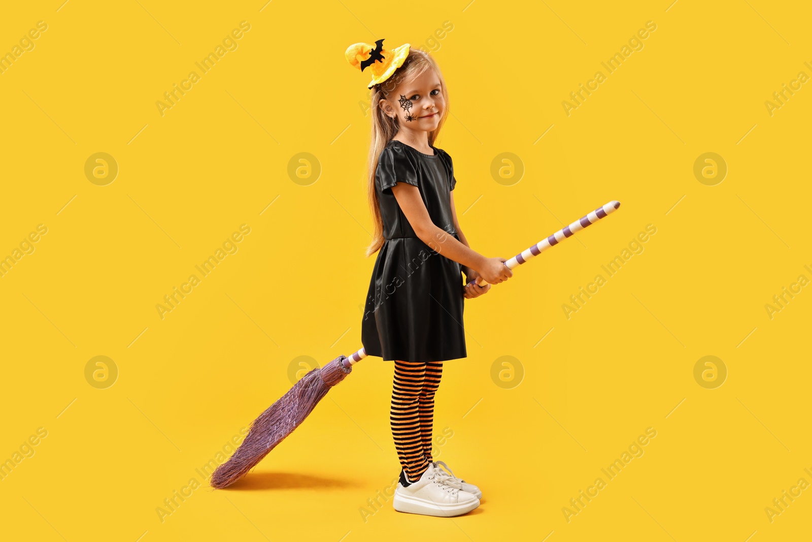 Photo of Funny girl with broom dressed like witch on yellow background. Halloween celebration