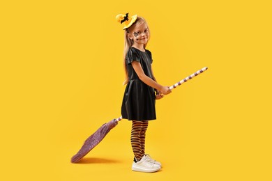 Funny girl with broom dressed like witch on yellow background. Halloween celebration