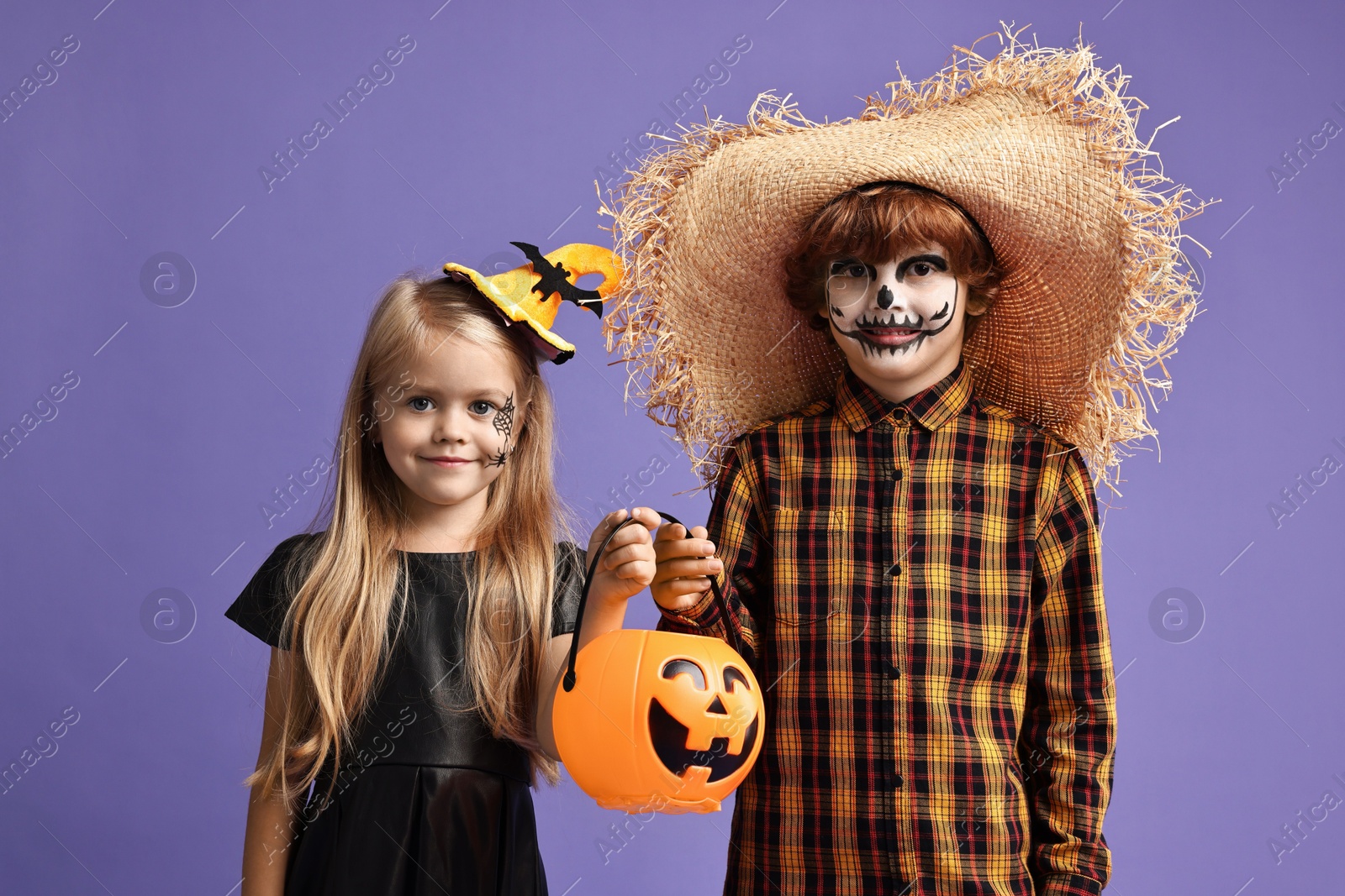 Photo of Cute children with pumpkin bucket wearing costumes on violet background. Halloween celebration