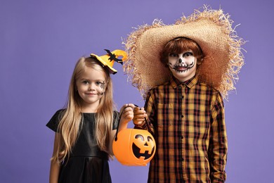 Photo of Cute children with pumpkin bucket wearing costumes on violet background. Halloween celebration