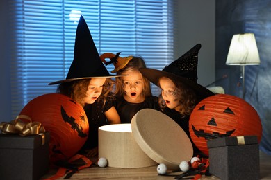 Surprised children in costumes with festive decor and gift boxes indoors at night. Halloween celebration