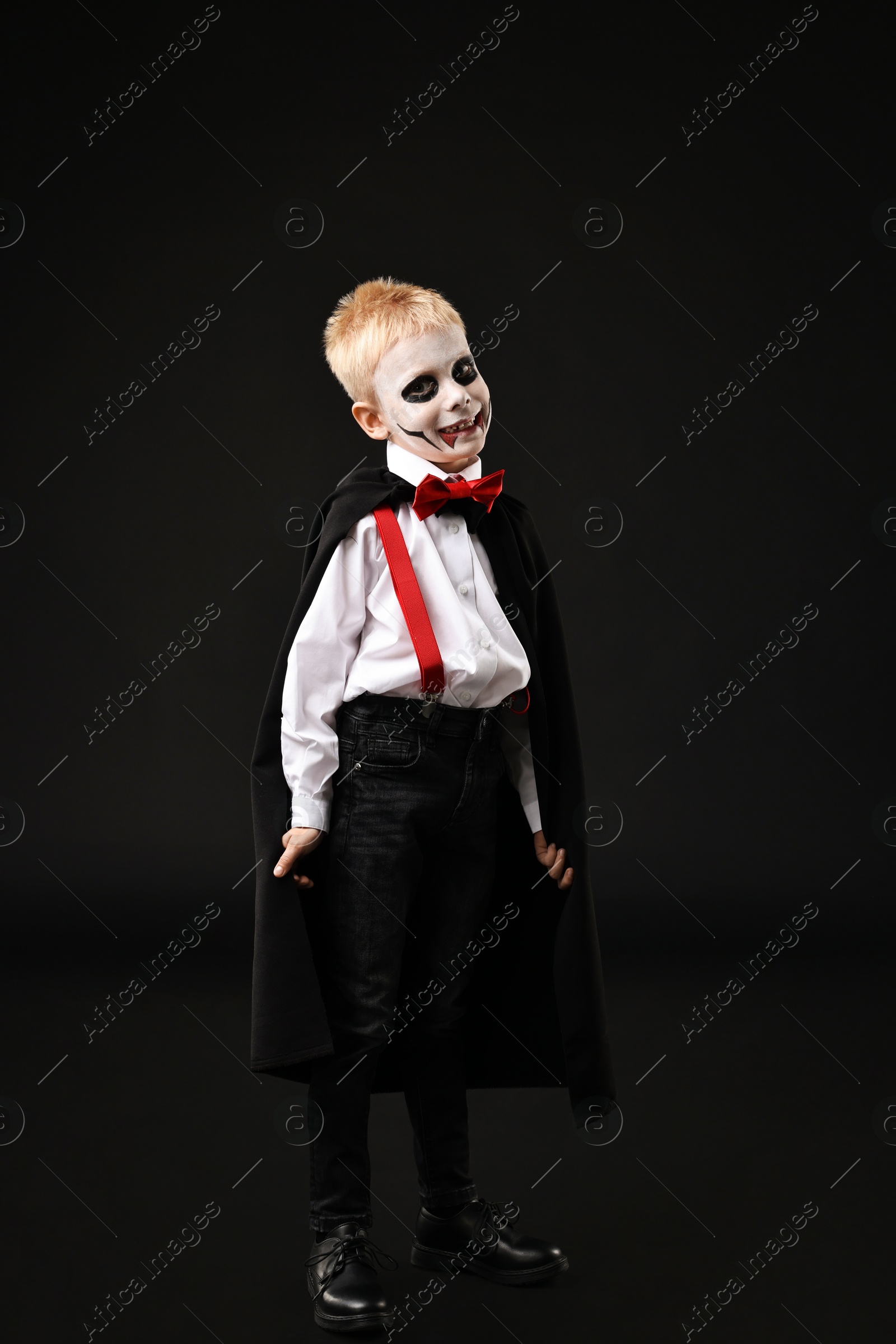 Photo of Funny boy dressed like vampire for Halloween celebration on black background