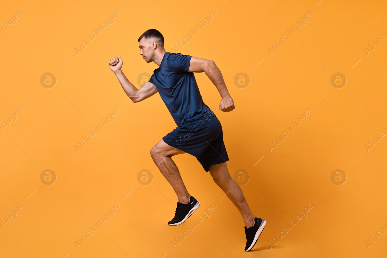 Photo of Man in sportswear running on orange background