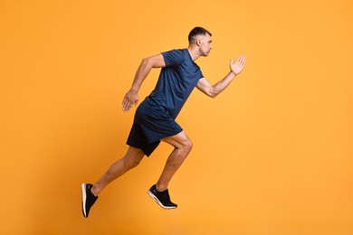 Photo of Man in sportswear running on orange background