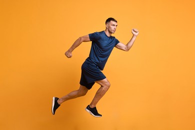 Photo of Man in sportswear running on orange background