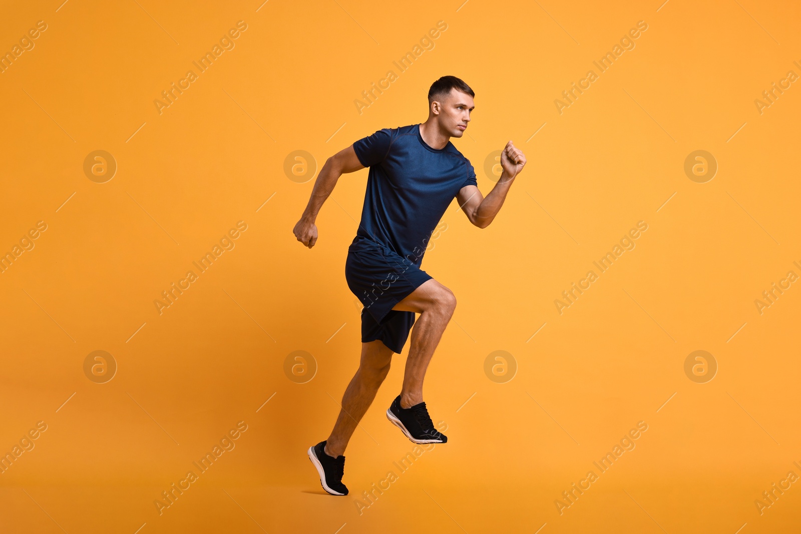 Photo of Man in sportswear running on orange background