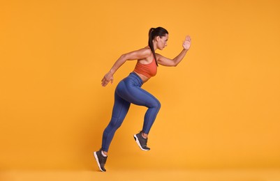 Photo of Woman in sportswear running on orange background