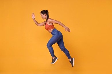 Photo of Woman in sportswear running on orange background