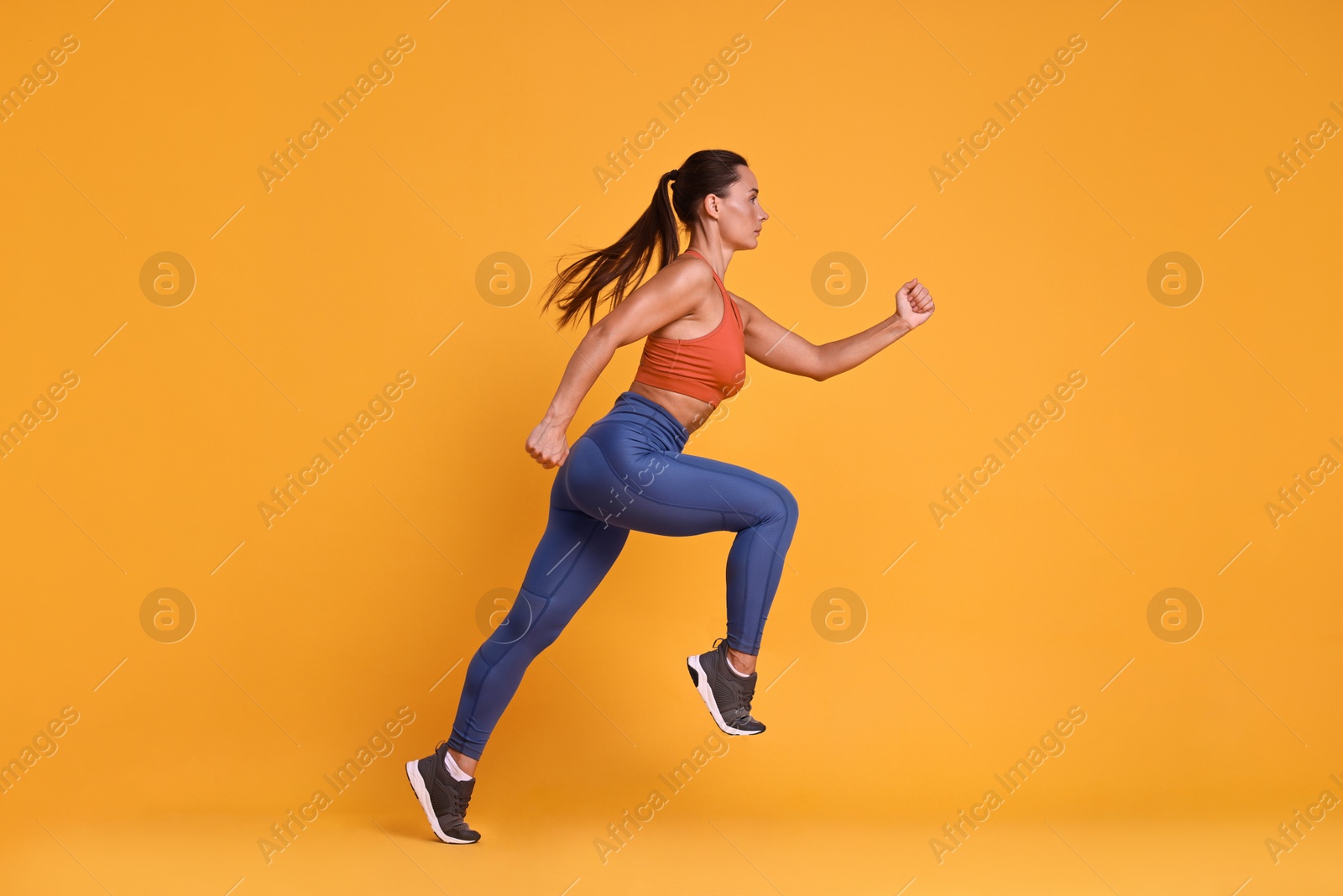 Photo of Woman in sportswear running on orange background