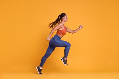 Woman in sportswear running on orange background