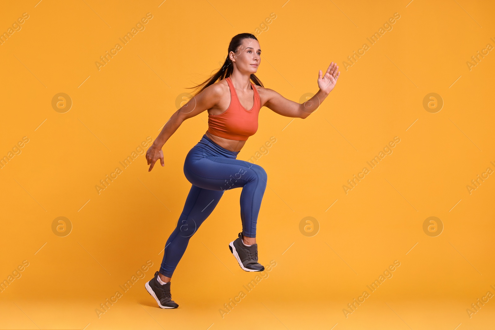 Photo of Woman in sportswear running on orange background