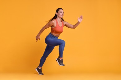 Woman in sportswear running on orange background