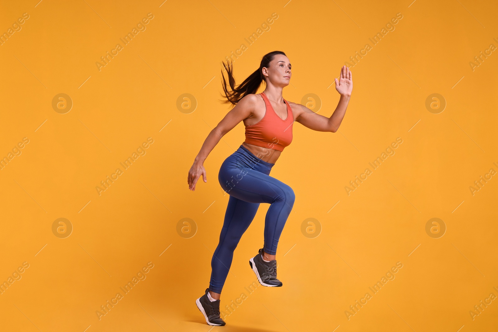 Photo of Woman in sportswear running on orange background